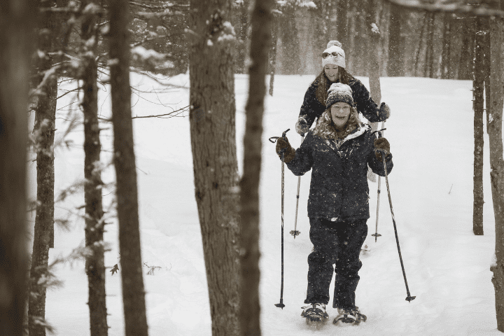 man and woman snowshoe in woods
