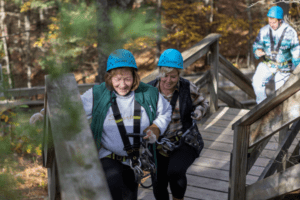 two women climb stairs to top of zip line
