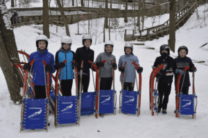 youth luge team standing with sleds